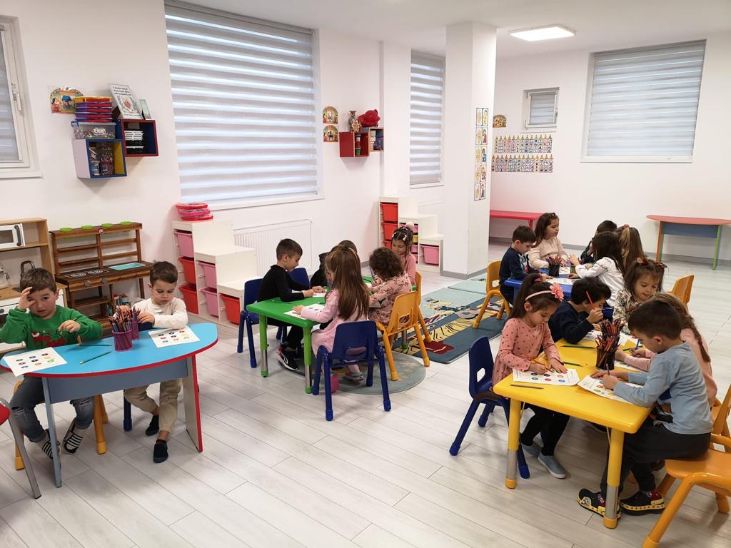 Copiii lucrează împreună la măsuțele colorate din sala de grupă.